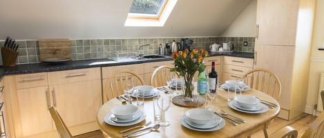 A dining area with a round wooden table set for four, surrounded by wooden chairs. A skylight above the table provides natural light.
