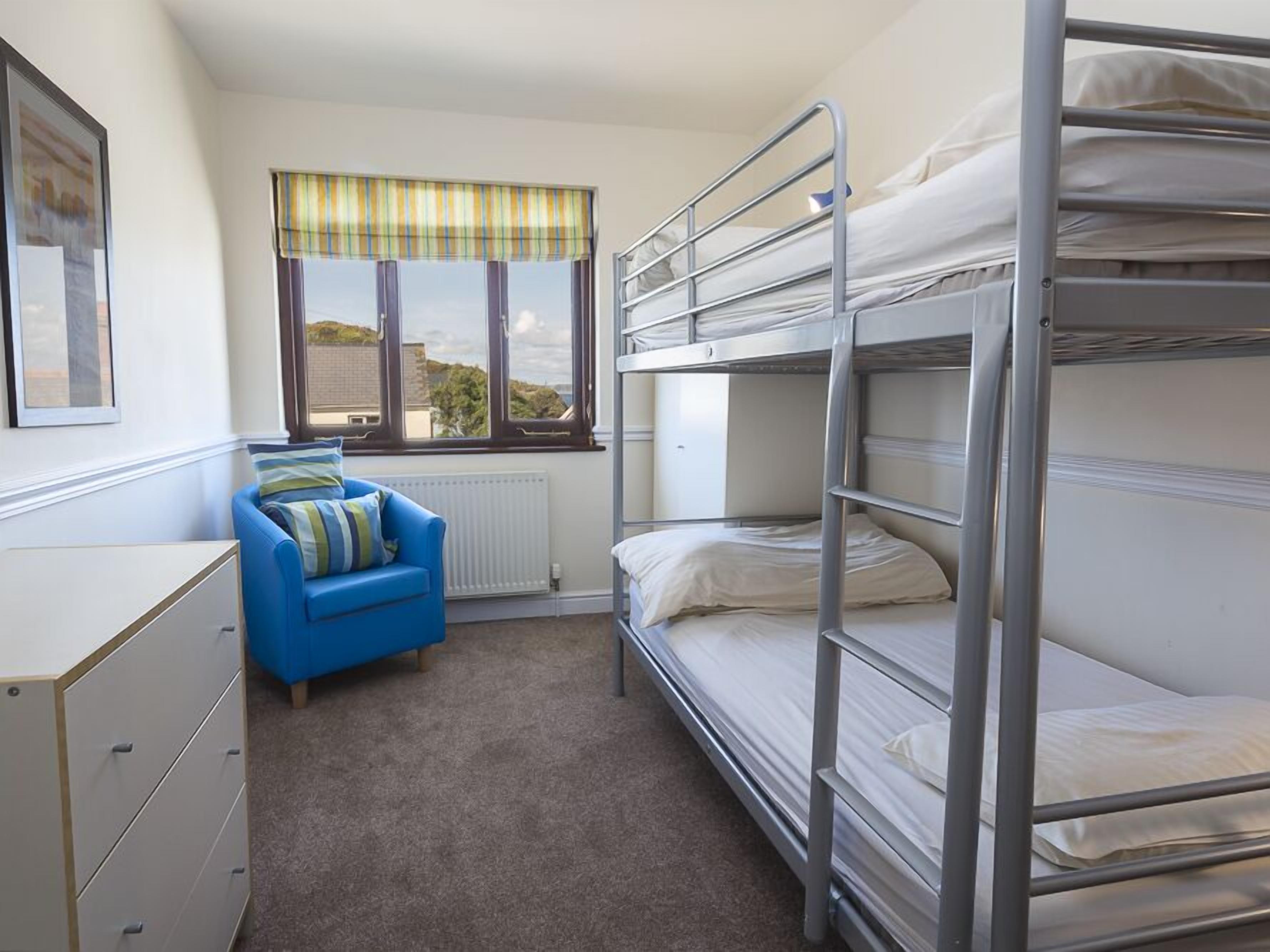 A bunk bed room with a blue chair, a radiator, and a window with a view of buildings.