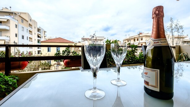 A bottle of Asti-al Nero wine and two glasses on a balcony table with a view of buildings. - Beating Heart City Family Home Next to Beach (Chania)