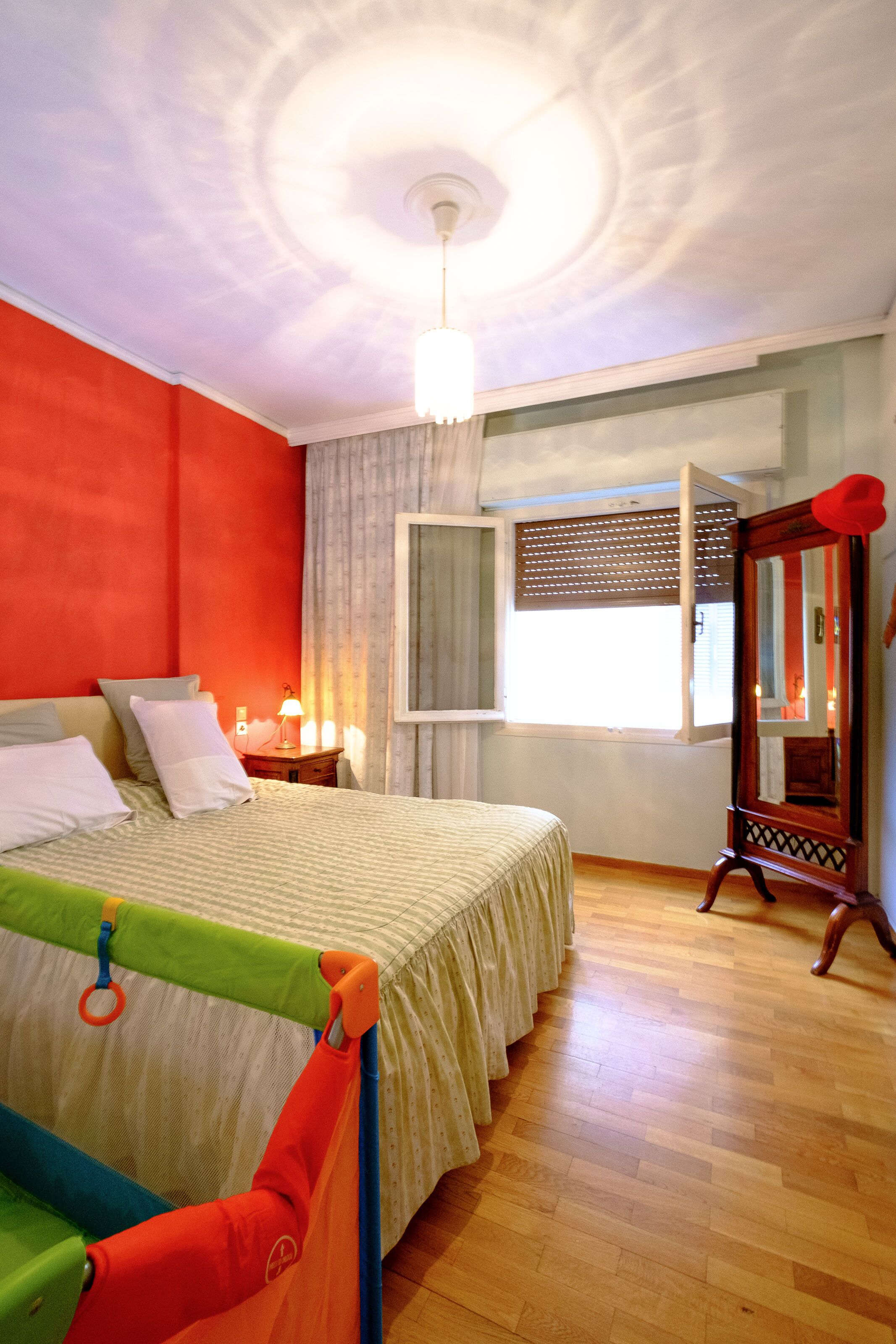 A bedroom with a bed, a nightstand, a window with blinds, a mirror, and a ceiling light fixture.