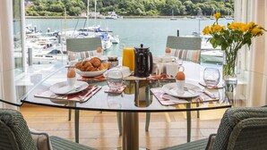 A dining table with breakfast items, a glass of orange juice, and a view of boats and greenery. - 7 Dart Marina (Dartmouth)