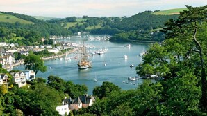 A coastal town with a marina filled with boats, surrounded by lush green hills and a clear sky. - 7 Dart Marina (Dartmouth)
