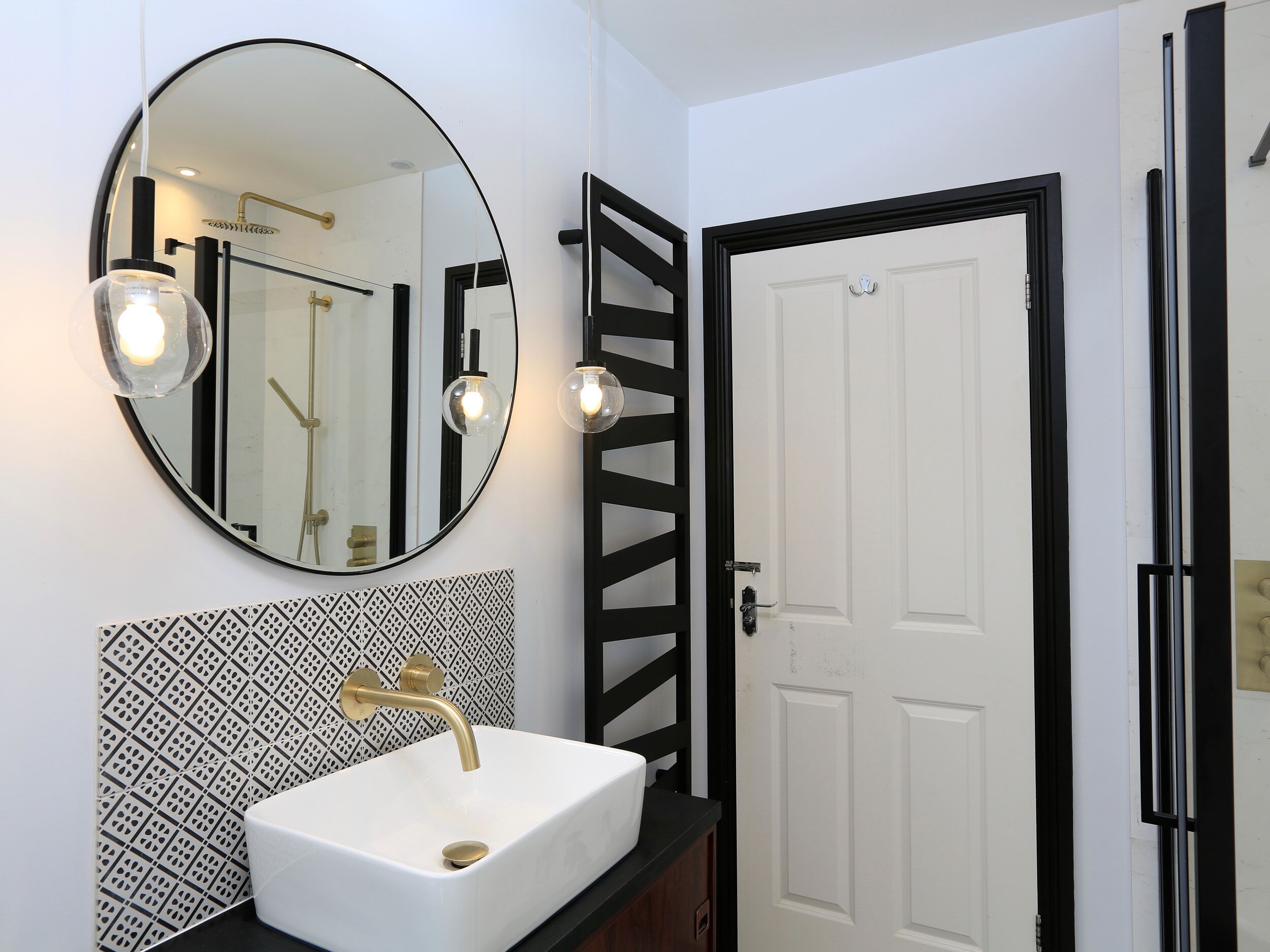 Un baño con un lavamanos blanco, un espejo redondo y una puerta con marco negro.