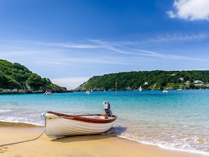 A boat tied to a sandy beach with clear turquoise water and green hills in the background.
