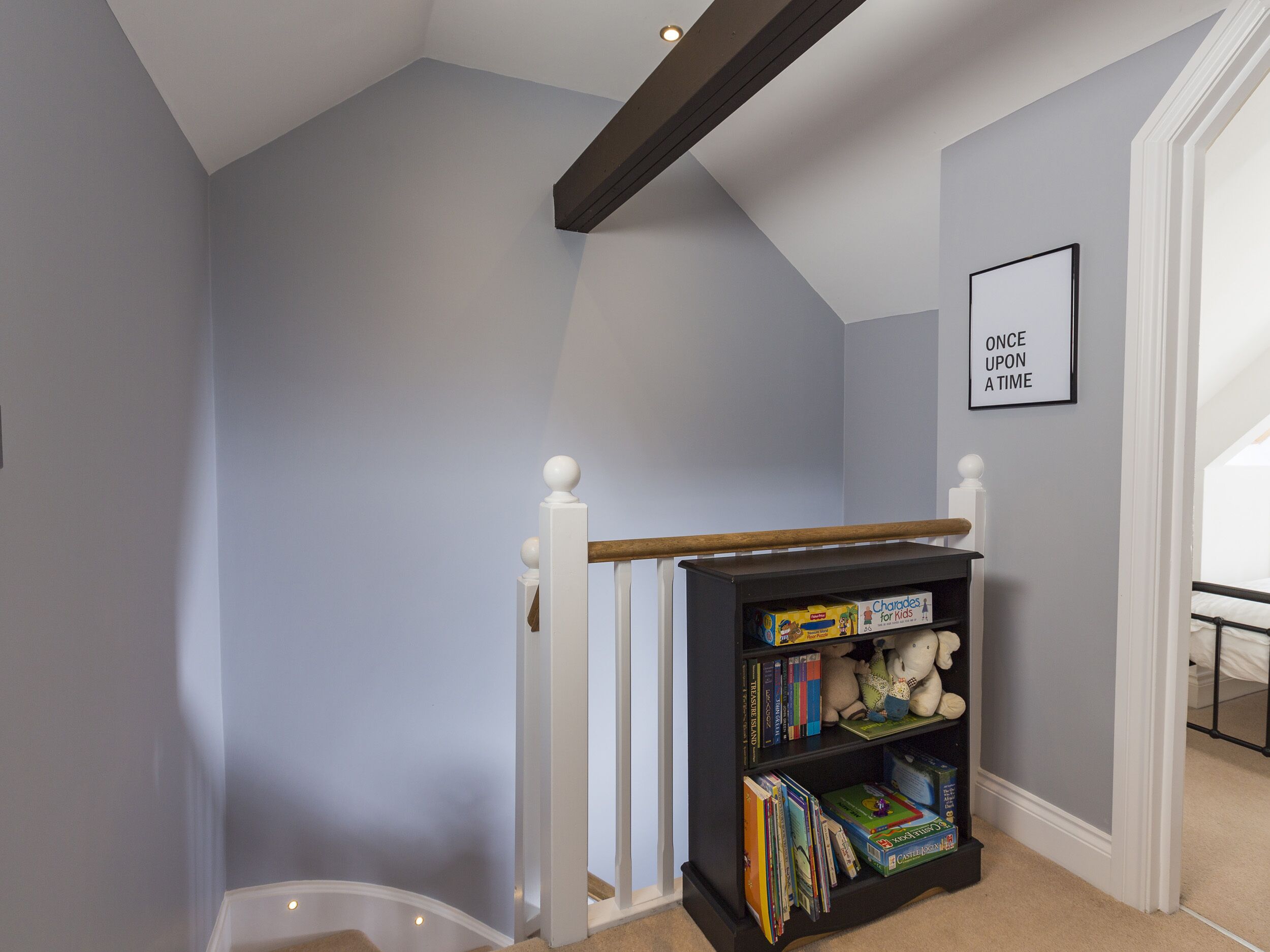 A staircase with a wooden handrail and a bookshelf filled with books and games.