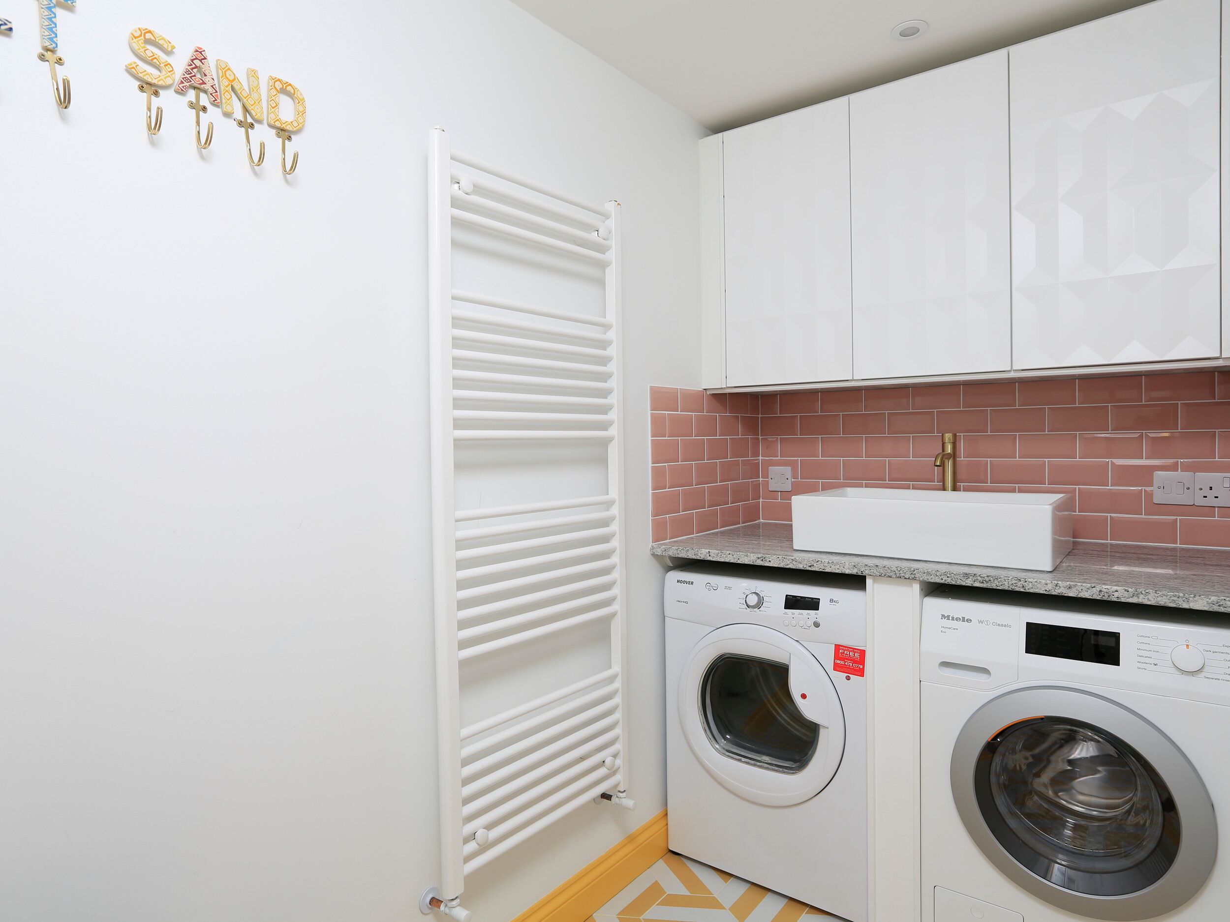 Un espace buanderie compact comprenant un lave-linge et un sèche-linge à chargement frontal, un radiateur blanc et un pare-feu en carrelage.