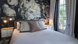 A bedroom with a large floral mural on the wall, a bed with white bedding, two bedside tables with lamps, and a window with curtains. - 16 Courtenay Street (Salcombe)