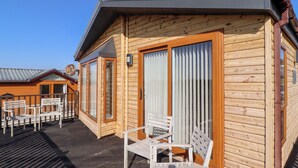Een houten chalet met een balkon, witte stoelen en een schuifdeur van glas.