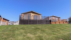 Een gelijkvloers houten huis met een omheind terras, gelegen tussen andere vergelijkbare huizen.