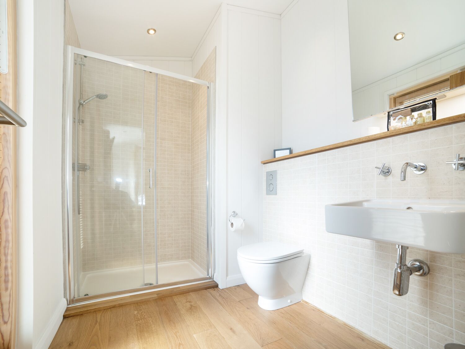 Un baño moderno con ducha de vidrio, inodoro blanco y lavamanos con espejo.