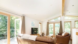 A spacious living room with a large leather sofa, a television, and a fireplace. - 7 Streamside (Looe)