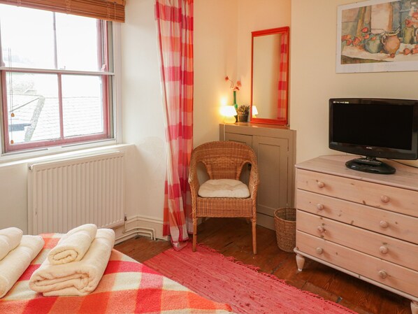 A bedroom with a bed, a chair, a dresser, a television, and a window with curtains.