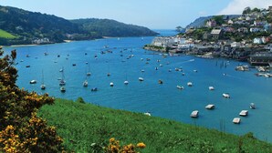 Une ville côtière où des bateaux sont amarrés le long du port, entourée d’une végétation luxuriante et de collines.