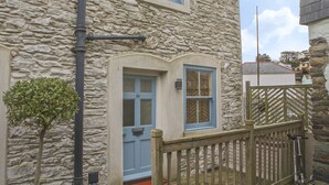 Un bâtiment en pierre avec une porte bleue et des volets aux fenêtres, un petit arbre et une clôture en bois.