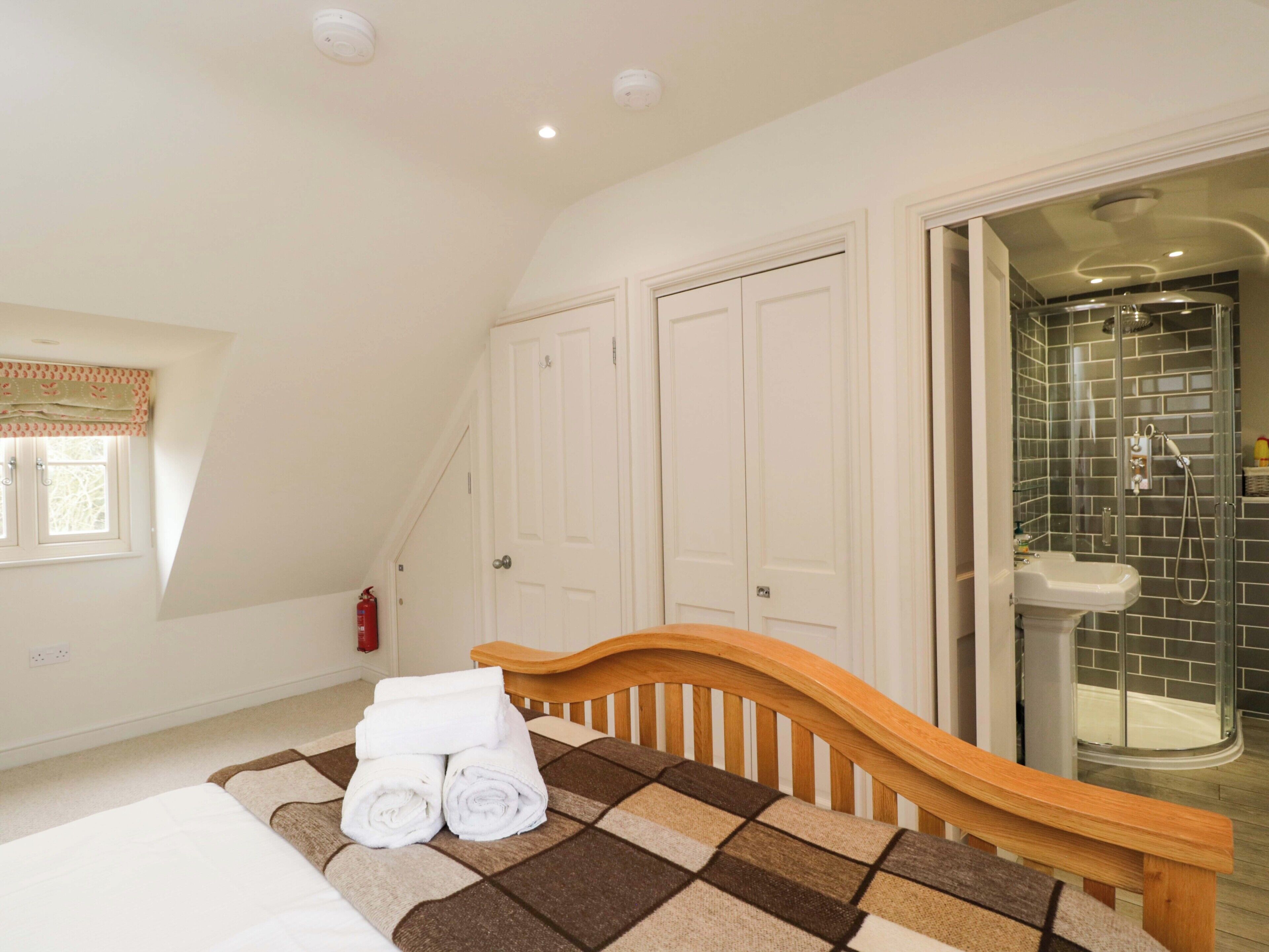 A bedroom with a bed, a wooden headboard, a window with a curtain, a closet with white doors, and a shower area with a glass door.
