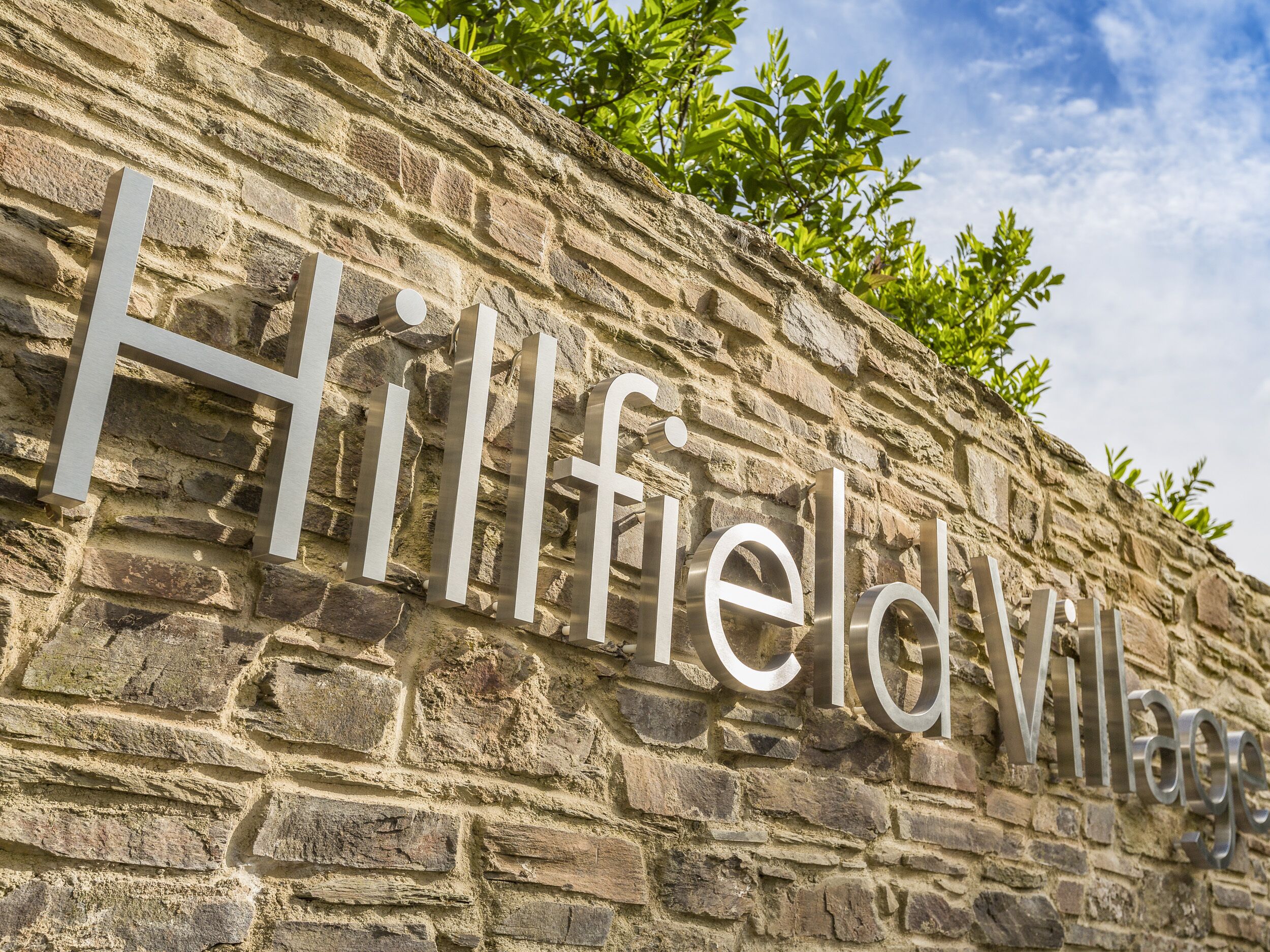A stone wall with the text "Hillfield Village" engraved on it.