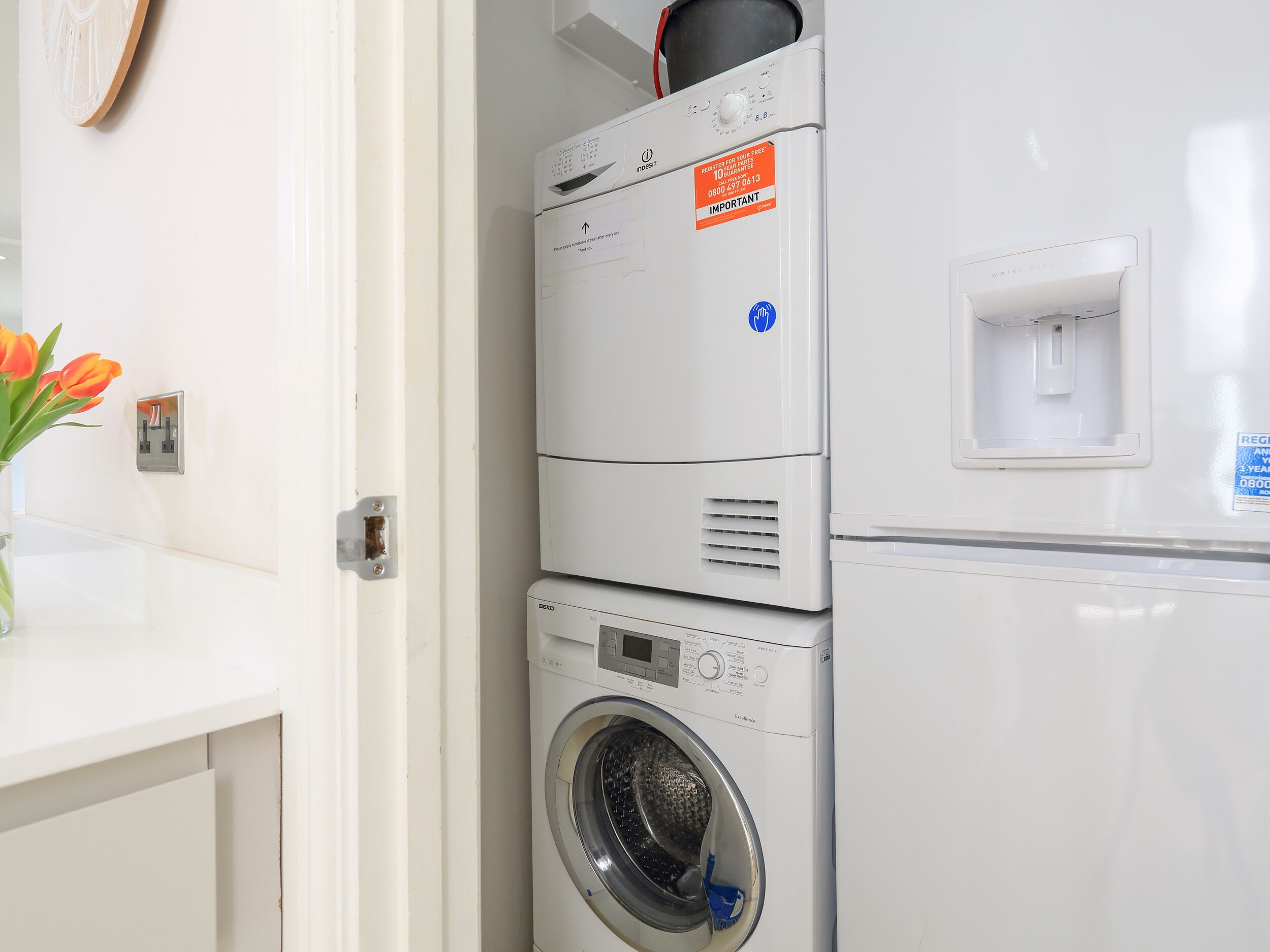 A stacked washer and dryer unit with a water inlet and a wall-mounted electrical outlet.