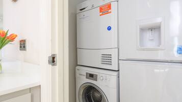 A stacked washer and dryer unit with a water inlet and a wall-mounted electrical outlet.