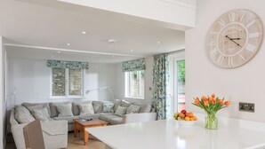 A modern living room with a large white island, a sofa, and a dining area. - Keepers Lodge, Hillfield Village (Dartmouth)