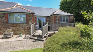 A stone and brick house with a wooden deck, a small garden, and a paved pathway. - Keepers Lodge, Hillfield Village (Dartmouth)