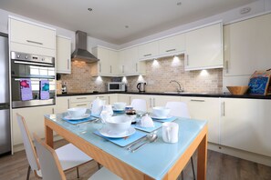 A modern kitchen with white cabinets, a glass dining table, and stainless steel appliances. - Normandy Watch (Salcombe)