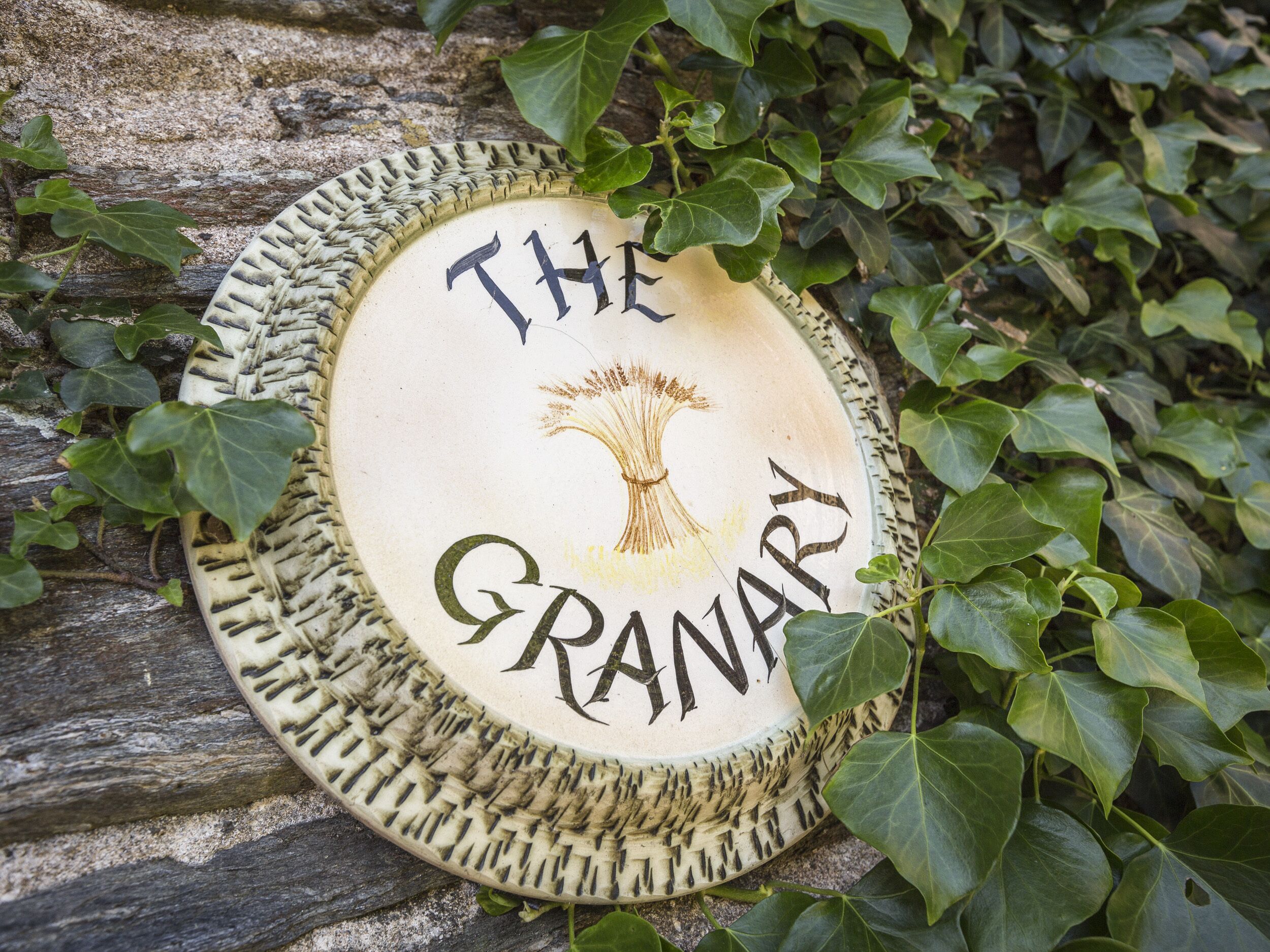 Un panneau circulaire portant l’inscription « The Granary » et illustré d’un arbre, le tout entouré de lierre.
