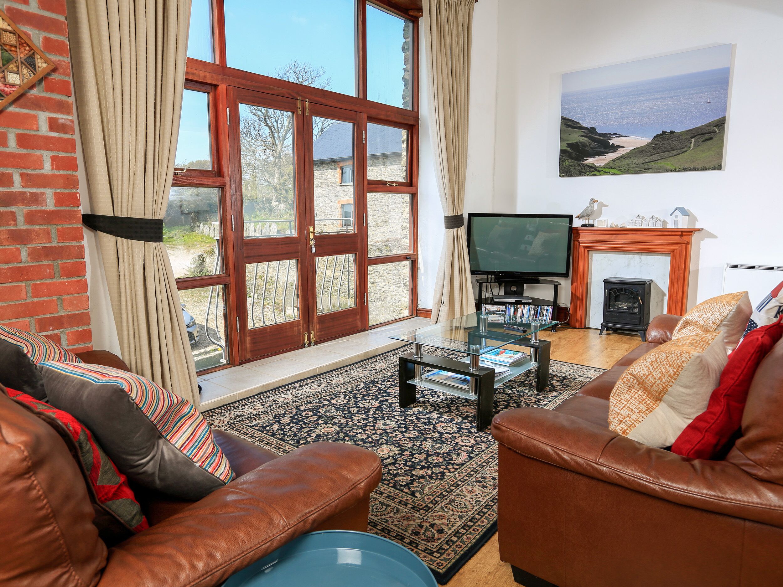 A living room with leather sofas, a glass coffee table, a television, a fireplace, and a large window with curtains.