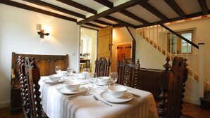 Un comedor con una mesa dispuesta para seis comensales, sillas de madera y una escalera al fondo.
