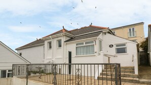 Une maison à deux étages, avec un toit recouvert de tuiles rouges, une façade blanche et une clôture en métal noir au premier plan.
