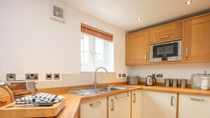 A modern kitchen with wooden cabinets, a stainless steel sink, a Bosch microwave, and a kettle.