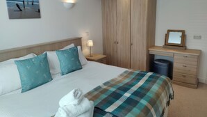 A neatly made bed with a checkered blanket, a bedside lamp, and a wall-mounted picture of a beach scene.