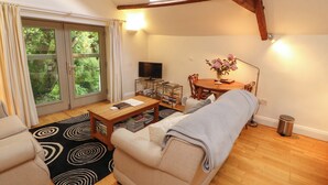 A living room with a sofa, a coffee table, a TV, and a dining table with chairs. - Holemire Barn (Cockermouth)