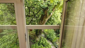 A view through a window with a wooden frame, a stone pathway, and dense green foliage. - Holemire Barn (Cockermouth)