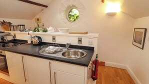 A kitchen with a central island, a built-in sink, and a window above the sink. - Holemire Barn (Cockermouth)