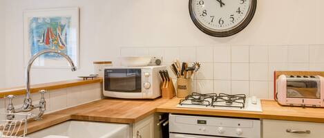 A kitchen with a microwave, toaster, gas stove, oven, sink, and a wall clock.
