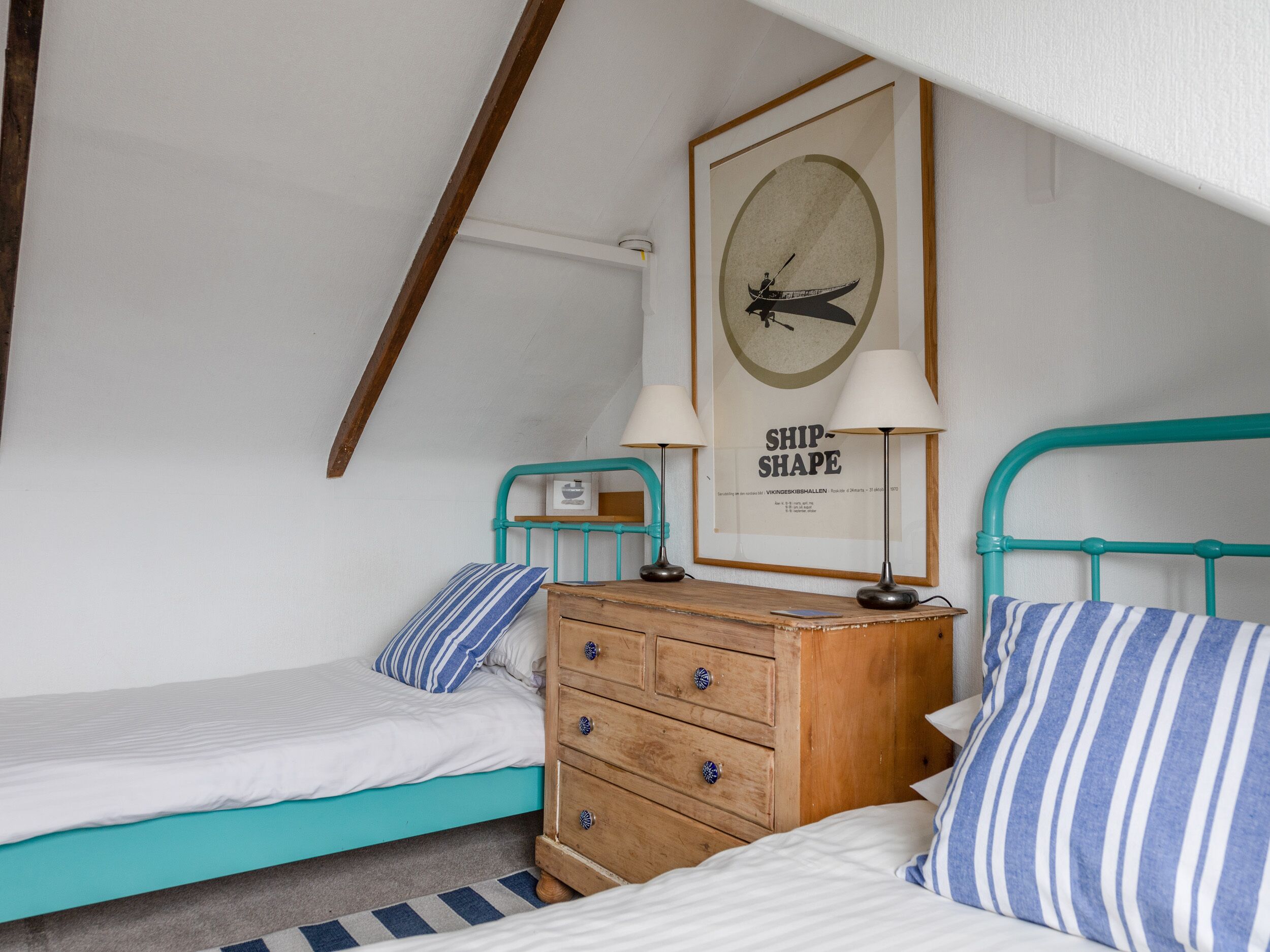 A small, cozy bedroom with two single beds, a wooden dresser, and a framed picture on the wall.