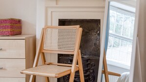 Een houten stoel met een geweven rugleuning en zitvlak, geplaatst voor een open haard met decoratieve haardmantel.