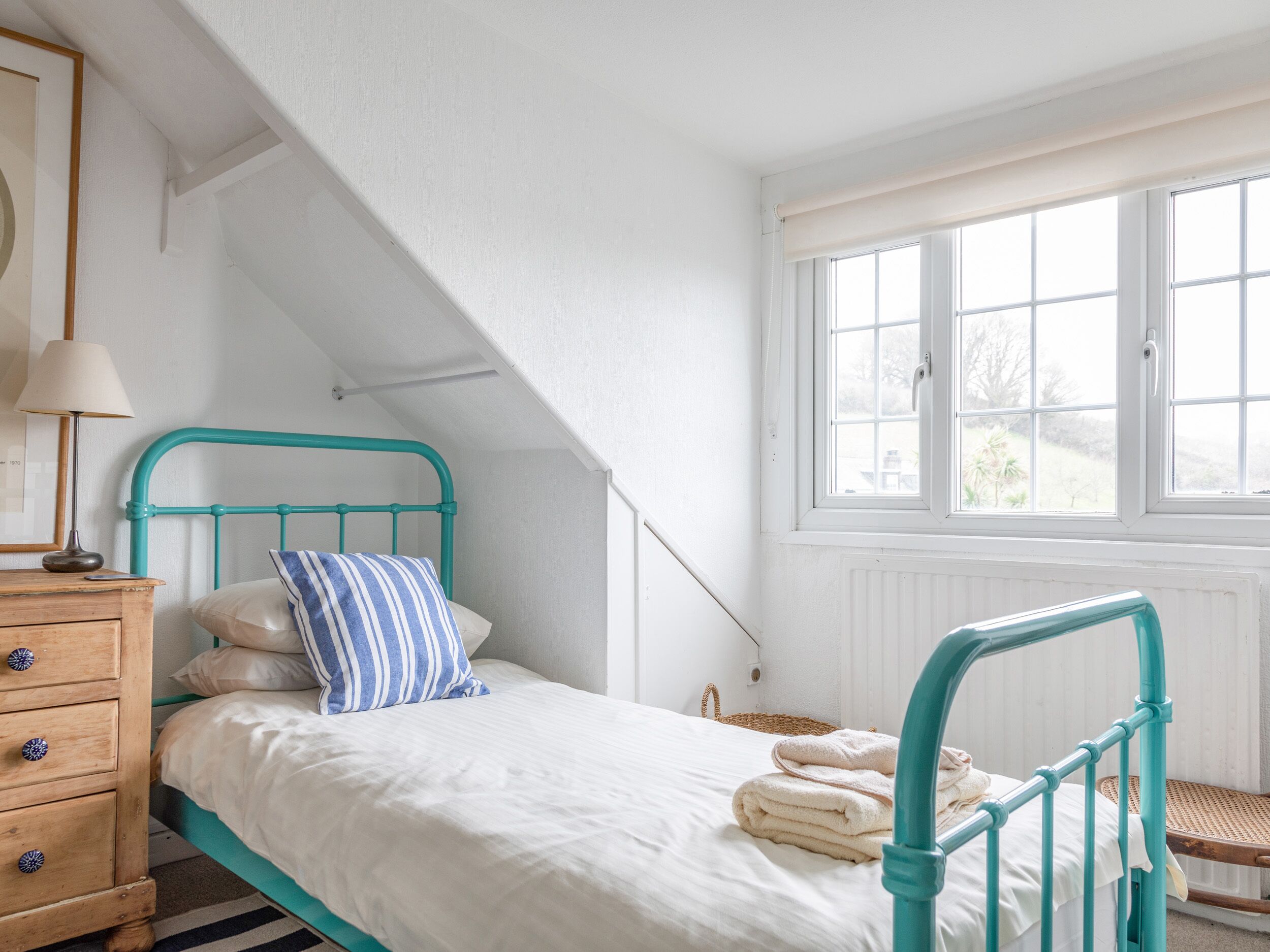 A bedroom with a bed, a wooden dresser, a window, and a view of the outdoors.