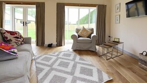 A spacious living room with a sofa, armchair, and a patterned rug. - Park Bothy (Cheltenham)