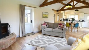 A spacious living area with a fireplace, a sofa set, a dining table with chairs, and a kitchen in the background. - Park Bothy (Cheltenham)
