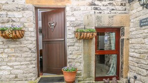 A stone building with a wooden door and a window, potted plants, and a rooster decoration.