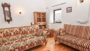 A living room with two sofas, a wooden cabinet, a clock, and a window.