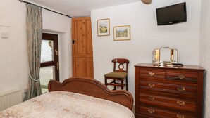 A bedroom with a bed, wooden dresser, and a television on the wall.