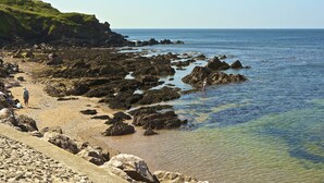 Une plage rocheuse avec une eau claire et un paysage vallonné en arrière-plan.