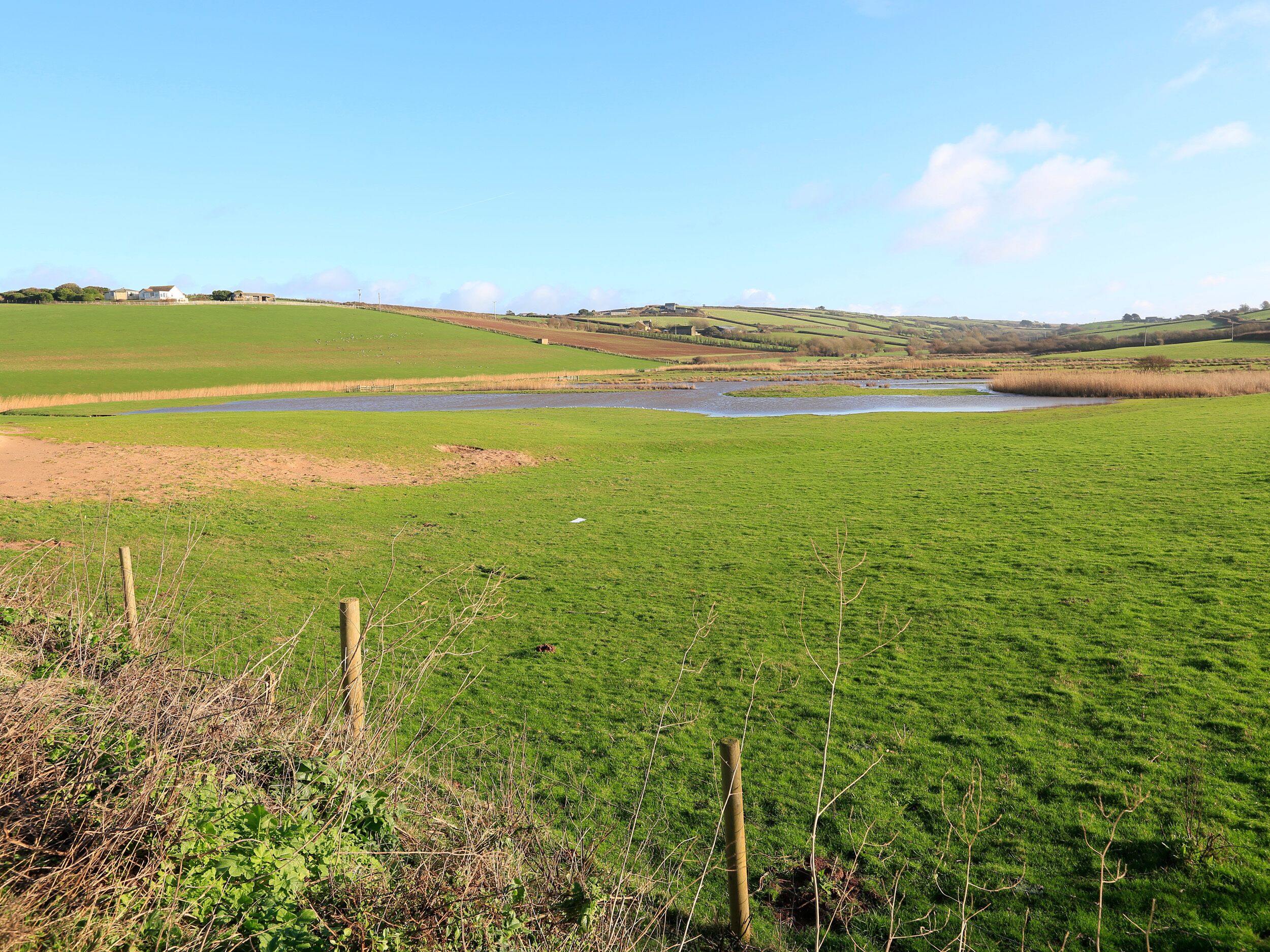 A rural landscape with a river, green fields, and distant hills.
