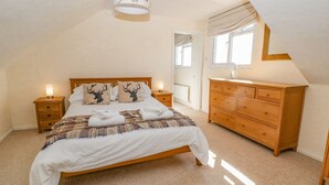Une chambre à coucher avec un lit en bois, deux tables de chevet avec des lampes, une commode en bois et une fenêtre avec des rideaux.