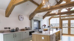 A modern kitchen with a central island, wooden beams, and a large window overlooking a balcony. - Butterwell Barn (Dartmouth)