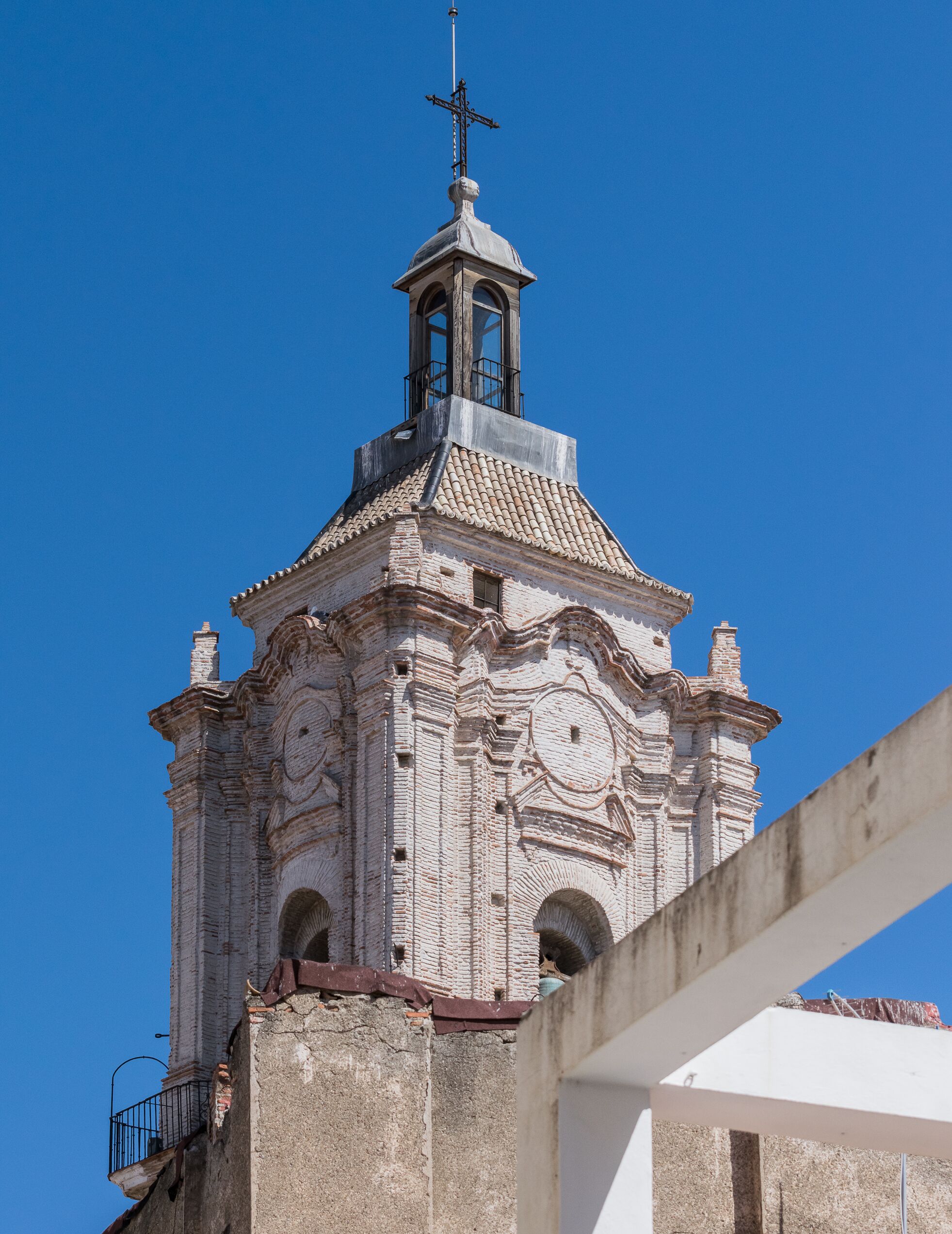 Ein historischer Kirchturm mit Kreuz auf der Spitze, detaillierter Steinmetzarbeit und rundbogigen Fenstern.