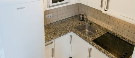 A compact kitchen with white cabinets, a built-in microwave, a stainless steel sink, and a stove.