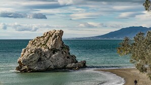 A rocky coastline with a large rock formation, a beach, and a distant mountain range. - Very bright apartment in the historic center - MALAMA B2  (Málaga)